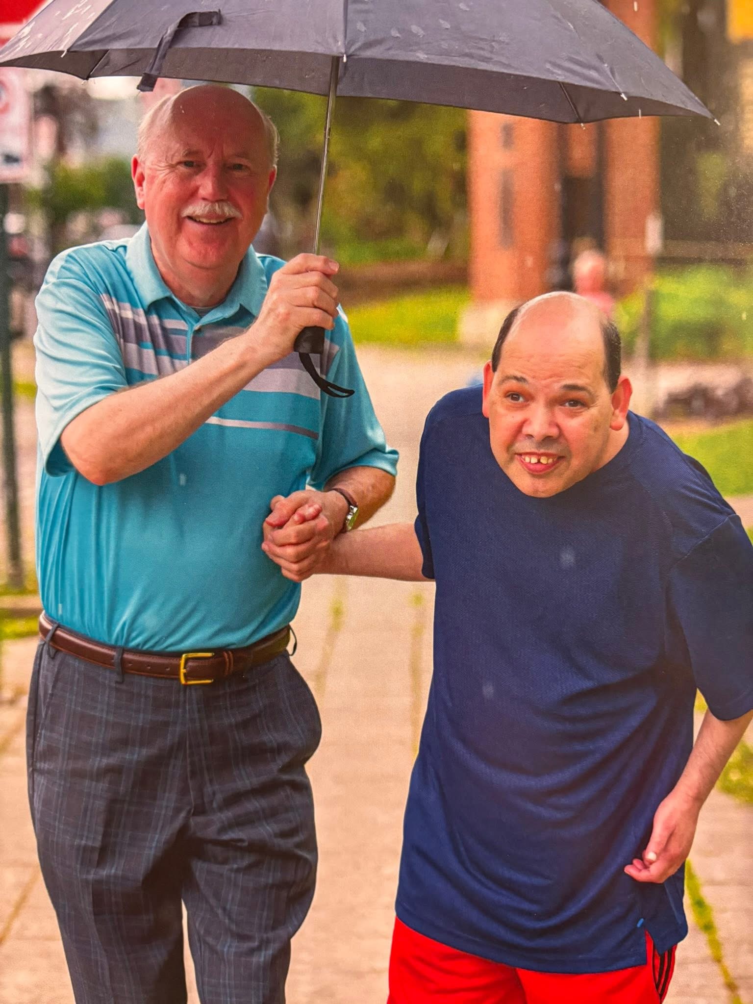 A Community Inclusion KY caregiver walking with a participant in the rain, sharing an umbrella